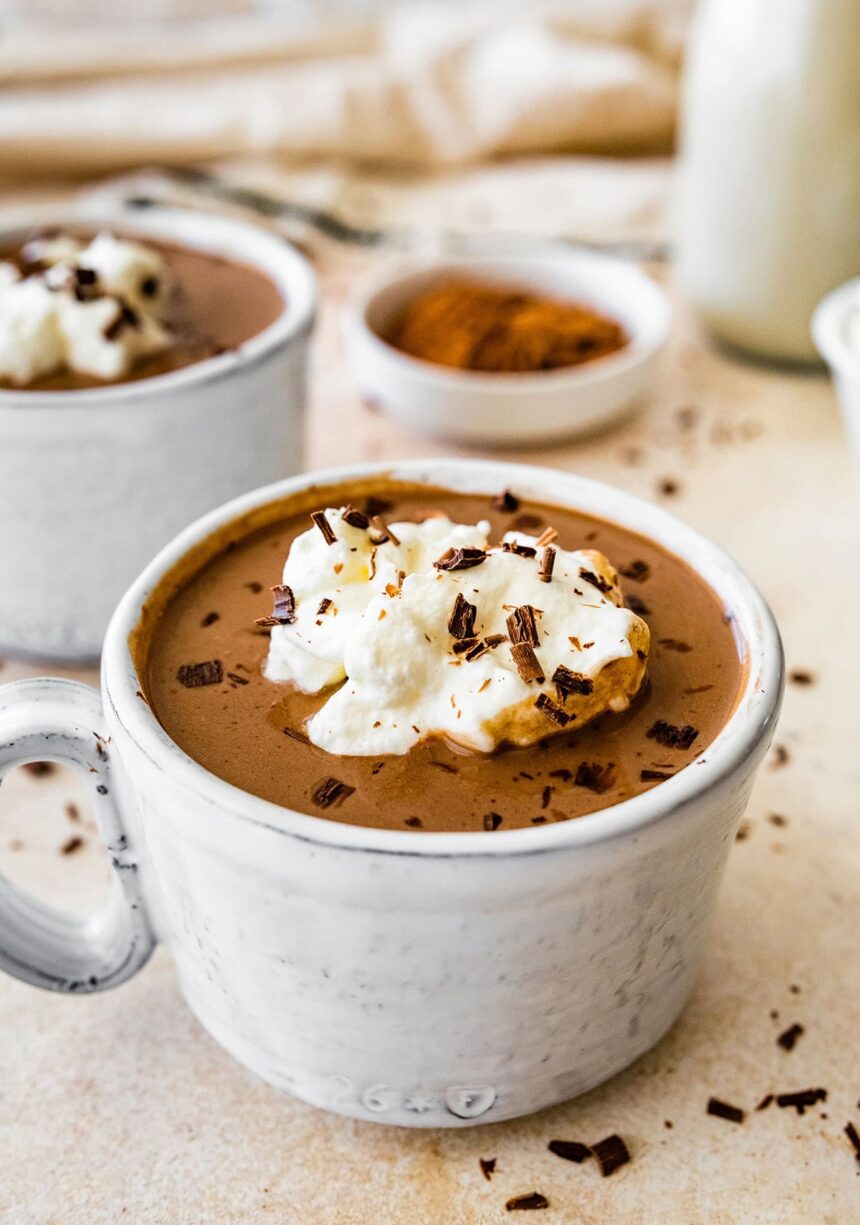 Protein hot chocolate in a white ceramic mug topped with whip cream and shaved chocolate.