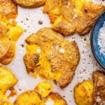 Seasoned and salted smashed potatoes on a baking tray.