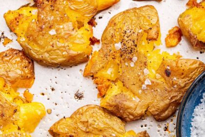 Seasoned and salted smashed potatoes on a baking tray.