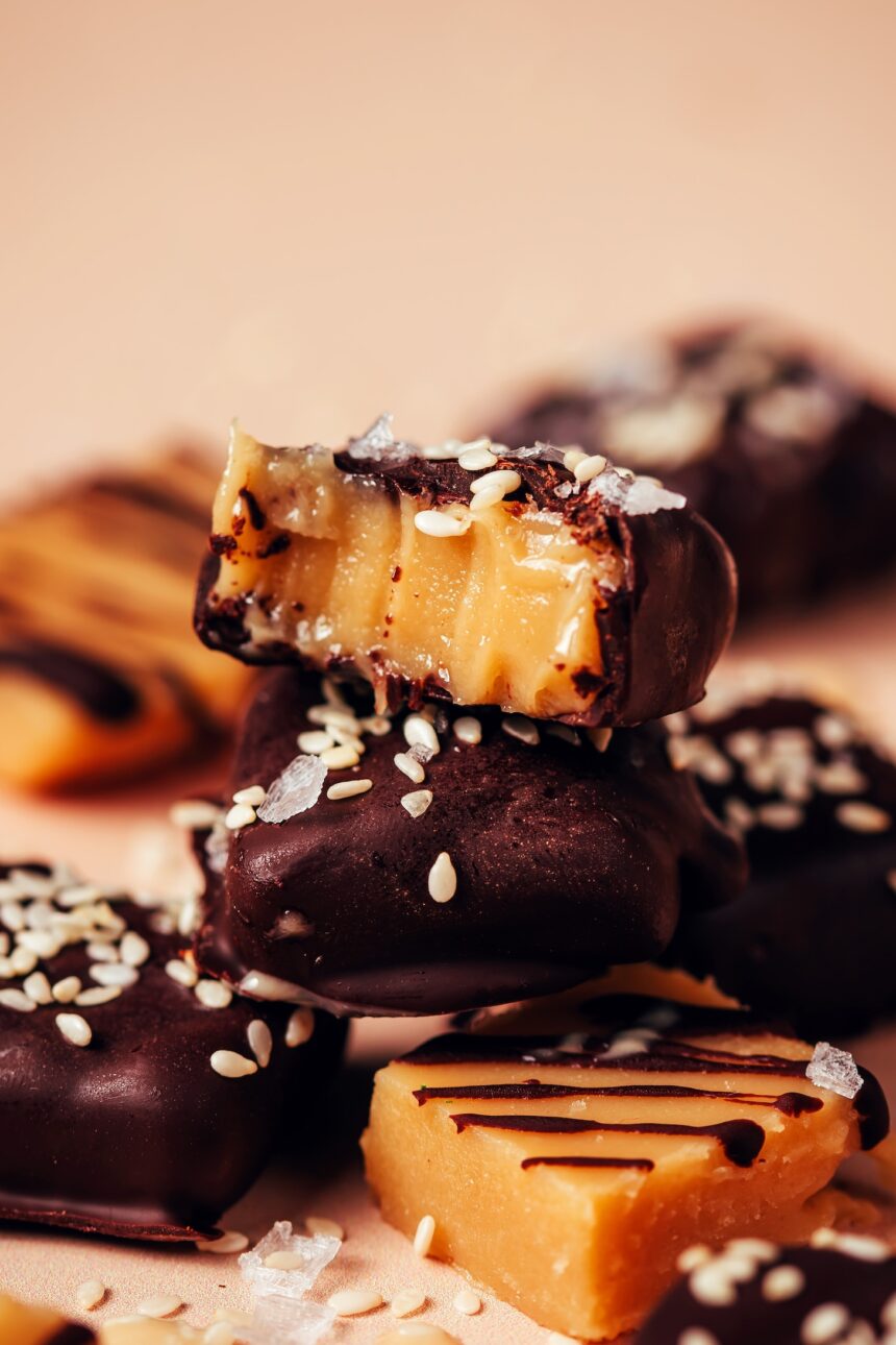 Close up shot of a stack of chocolate sea salt caramels with the top one partially eaten to show the soft, tender texture