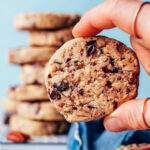 Holding up a vegan gluten-free chocolate chip pecan shortbread cookie with a stack of cookies behind it