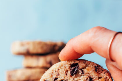 Holding up a vegan gluten-free chocolate chip pecan shortbread cookie with a stack of cookies behind it