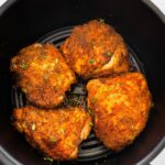 Four bone-in chicken thighs cooked in the basket of an air fryer topped with fresh parsley.