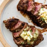 Two filet mignon pieces sliced on a white plate topped with garlic butter.