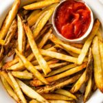 A plate of air fryer french fries with a small container of ketchup on the side.