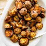 Crispy air fryer potatoes on a white plate garnished with fresh herbs and flaky sea salt.