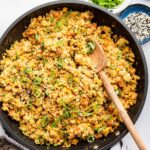 Cauliflower fried rice with eggs in a skillet with a wooden serving spoon. The dish is garnished with fresh green onion.