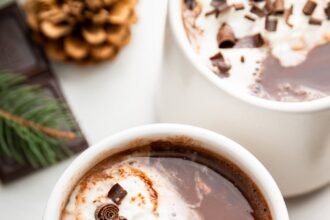 Two white mugs of hot chocolate topped with a little whip cream and chocolate shavings.