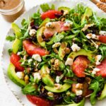 A salad with arugula, avocado, blue cheese, grapefruit, nuts, and cranberries on a white plate.