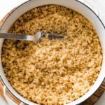 A large white pot filled with cooked quinoa. There is a silver fork in the quinoa.