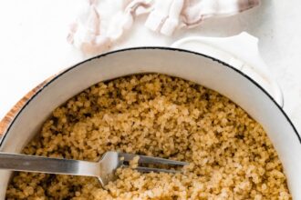 A large white pot filled with cooked quinoa. There is a silver fork in the quinoa.