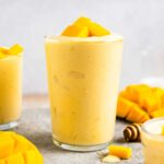 side view of a mango smoothie in a glass with mango chunks on top.