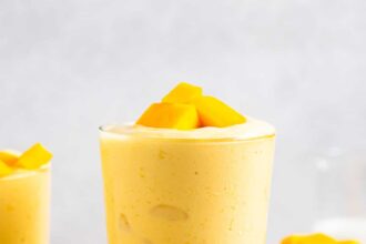 side view of a mango smoothie in a glass with mango chunks on top.