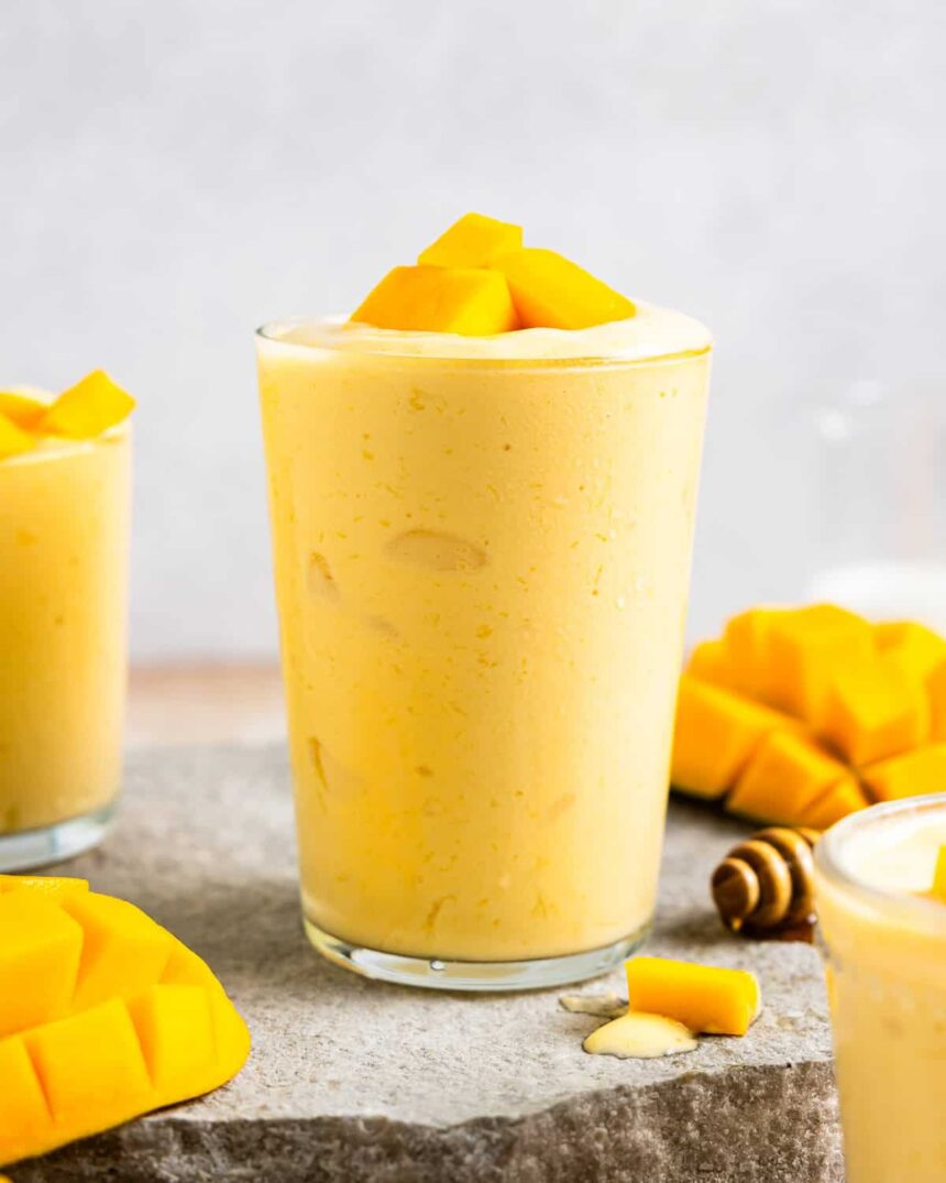 side view of a mango smoothie in a glass with mango chunks on top.