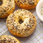 Four everything bagels on a gold cooling rack.