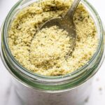 A vegan parmesan cheese made with hemp seeds in a glass mason jar with a metal spoon.