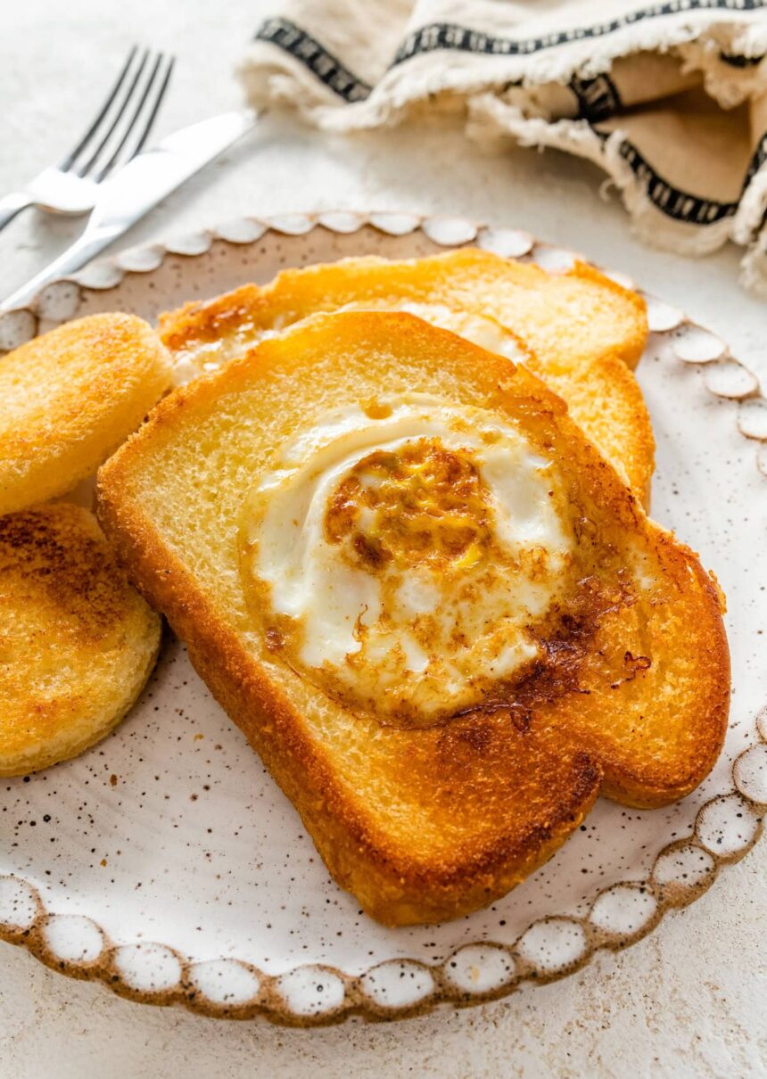 A slice of toast on a plate with the center cut out of it. A cooked egg is in the center of the slice of bread.