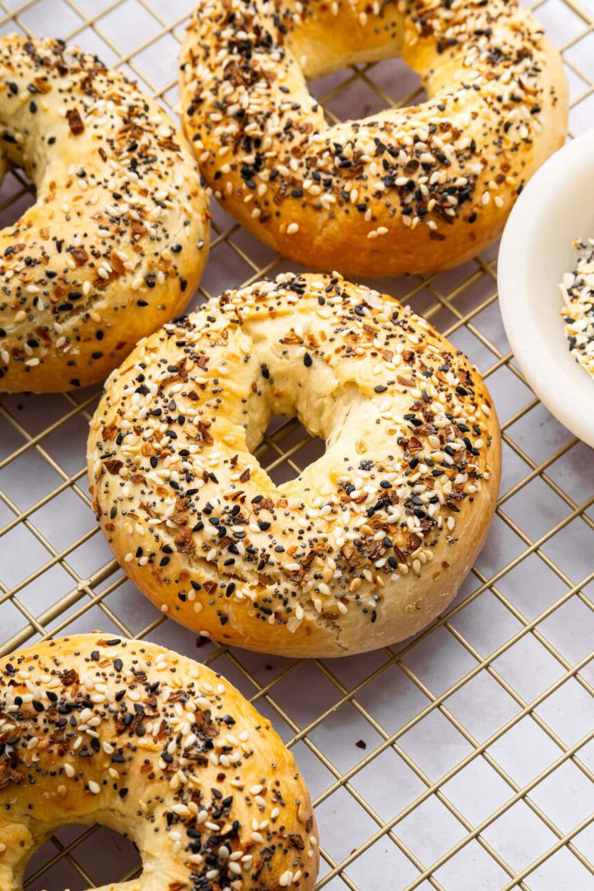 Four everything bagels on a gold cooling rack.