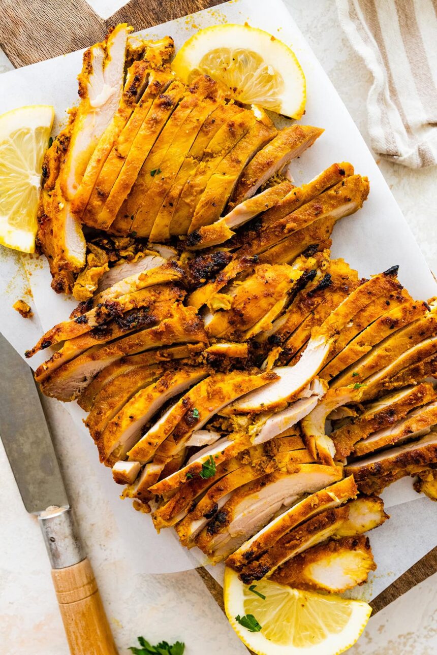 Chicken Shawarma sliced on a cutting board. There is a knife and lemon slices next to the chicken.