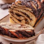 A chocolate babka on a long plate with a slice cut from the end.