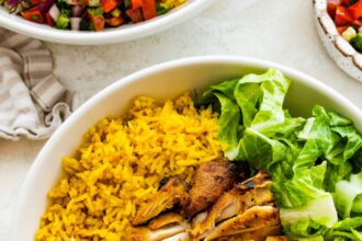 A chicken shawarma bowl with turmeric rice, sliced chicken shawarma, romaine lettuce, Shirazi salad, hummus and Toum.