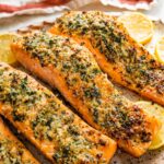 Four parmesan crusted salmon filets served on a speckled tray with multiple lemon slices.