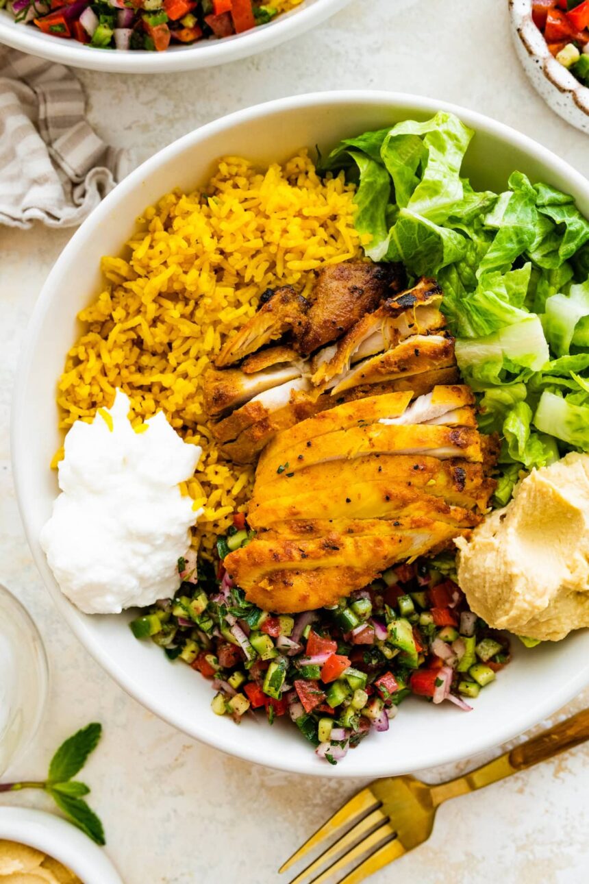 A chicken shawarma bowl with turmeric rice, sliced chicken shawarma, romaine lettuce, Shirazi salad, hummus and Toum.