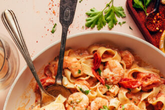 Serving spoons resting in a skillet of our dairy-free Tuscan shrimp pasta recipe