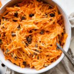 A carrot raisin salad in a white bowl with a spoon.