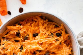 A carrot raisin salad in a white bowl with a spoon.