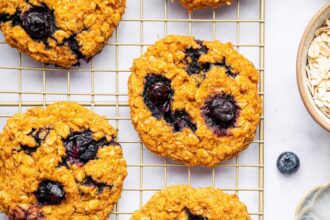 Six sweet potato blueberry oatmeal cookies on a wire cooling rack. Fresh blueberries are scattered next to the rack.