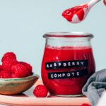 Spoonful of raspberry compote over a jar of compote with fresh raspberries next to it