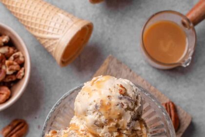 Overhead view of scoops of butter pecan ice cream in a glass dessert bowl, surrounded by ingredients.