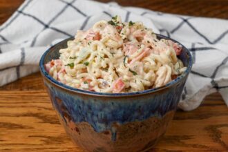 shrimp pasta salad in a pottery bowl with a white and blue patterned linen
