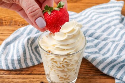 whipped cream in glass with strawberry dipping into it