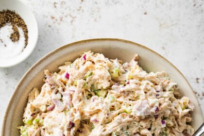 Cottage cheese chicken salad served in a cream bowl with a spoon. There is a small bowl with salt and pepper next to it.