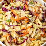 multi color Asian cabbage salad in a white bowl on a wooden surface with a blue and white linen