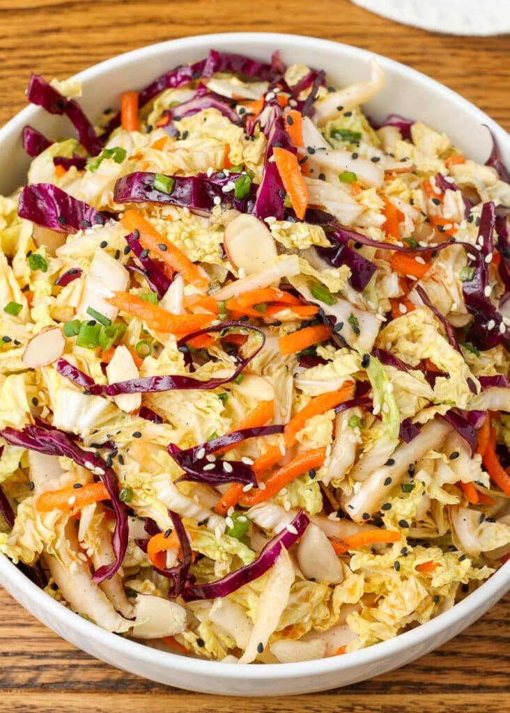 multi color Asian cabbage salad in a white bowl on a wooden surface with a blue and white linen