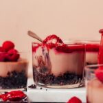 Glass dessert jars of our no-bake chocolate cheesecake cups with some topped with raspberries and others raspberry compote