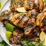 Cooked cilantro lime chicken thighs served on a plate topped with fresh cilantro and lime wedges.