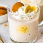 High-protein banana pudding in a glass topped with whipped cream, sliced bananas and a wafer cookie.