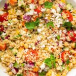 A mixed quinoa chickpea salad with tomatoes, cucumbers, feta, and parsley, in a white bowl.