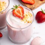 One glass filled with high-protein strawberry mousse topped with a dollop of cocowhip, one halved fresh strawberry and crushed graham crackers.
