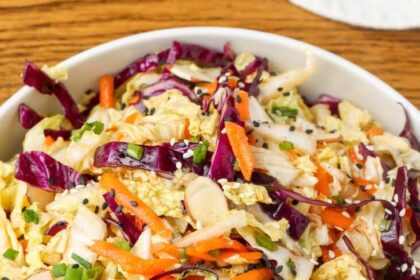 multi color Asian cabbage salad in a white bowl on a wooden surface with a blue and white linen