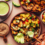 Drizzling green tahini sauce onto a Jerk Tofu & Roasted Plantain Bowl