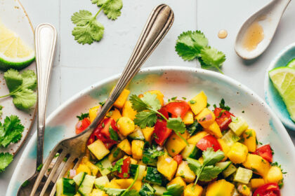 Fork and spoon resting in a bowl of Mango Cucumber Salad with lime wedges on top