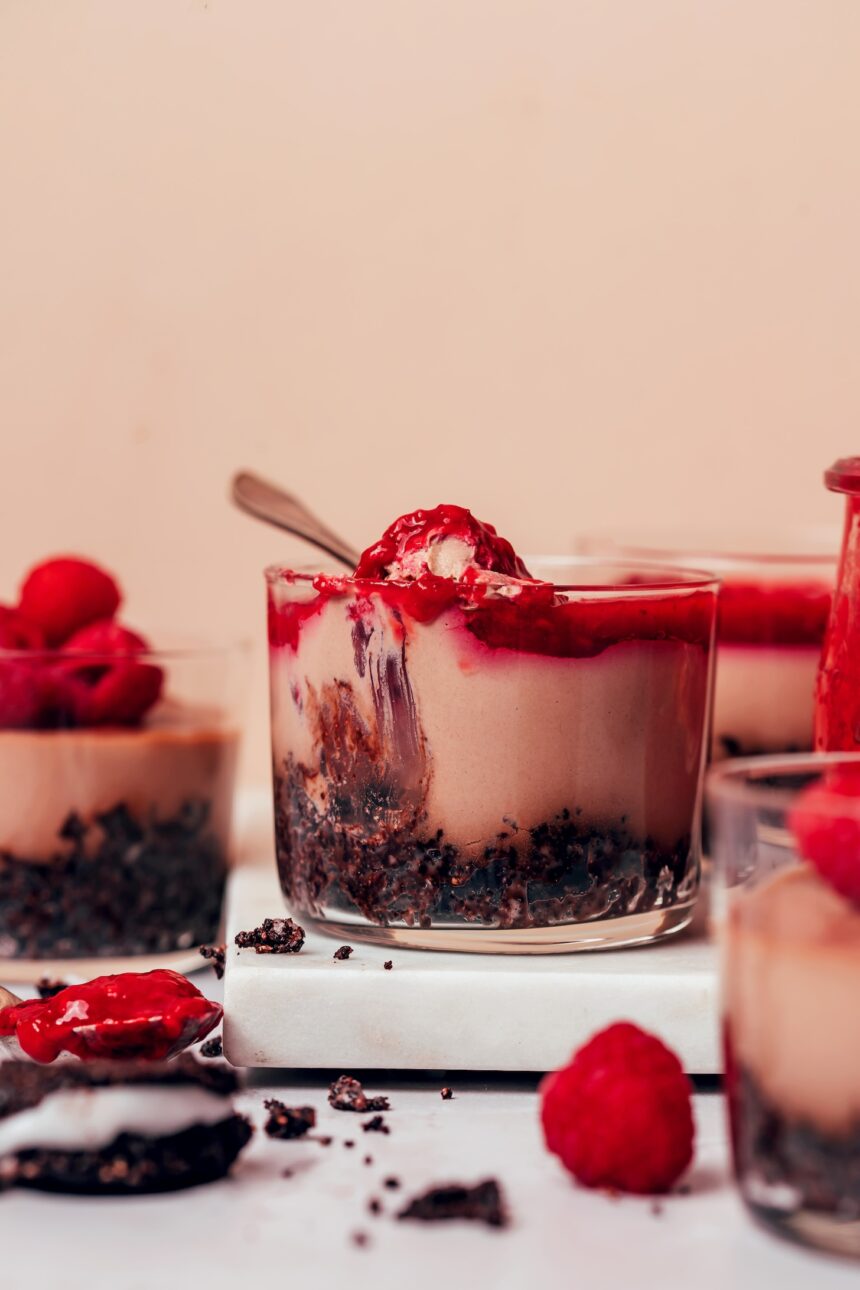 Glass dessert jars of our no-bake chocolate cheesecake cups with some topped with raspberries and others raspberry compote
