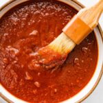 A bowl filled with homemade BBQ sauce with a small brush in the sauce.