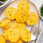 12 cottage cheese egg bites on a white serving plate topped with chopped chives. There are two forks on the plate.