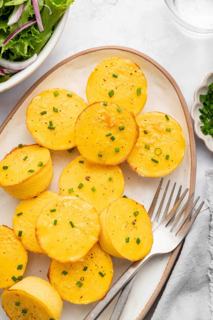 12 cottage cheese egg bites on a white serving plate topped with chopped chives. There are two forks on the plate.